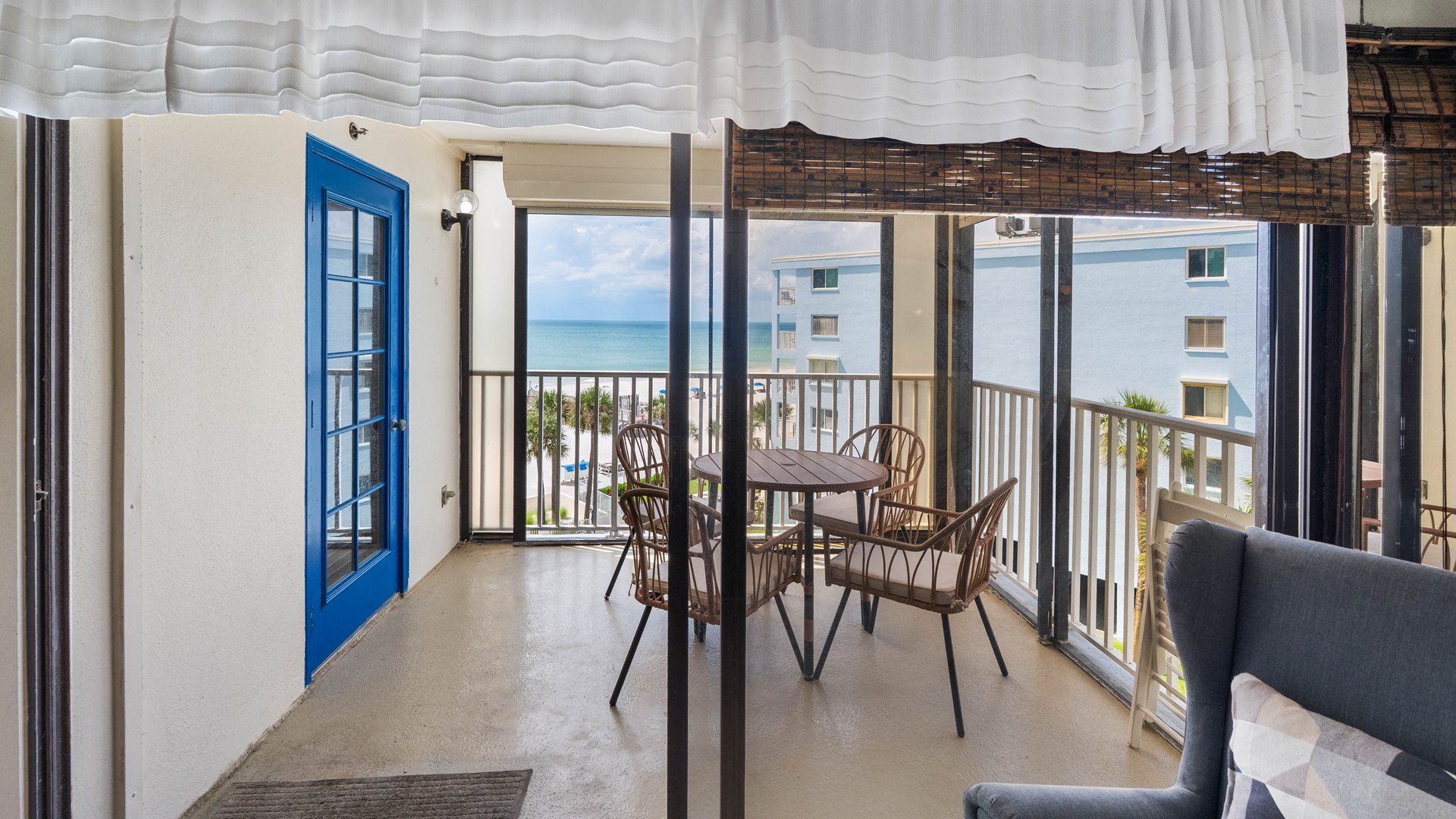 Un balcón con vistas al mar, una puerta azul y una mesa con sillas.