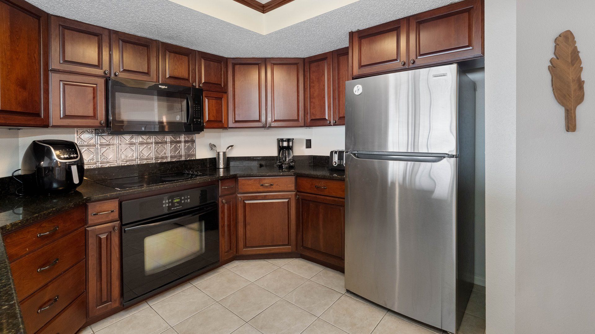 Una cocina con gabinetes de madera, un refrigerador de acero inoxidable, un microondas, una cafetera y un tostador.