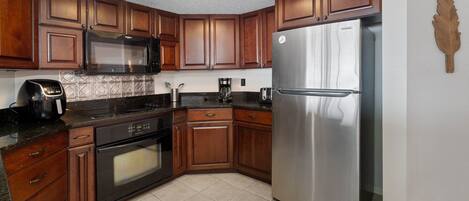 Una cocina con gabinetes de madera, un refrigerador de acero inoxidable, un microondas, una cafetera y un tostador.