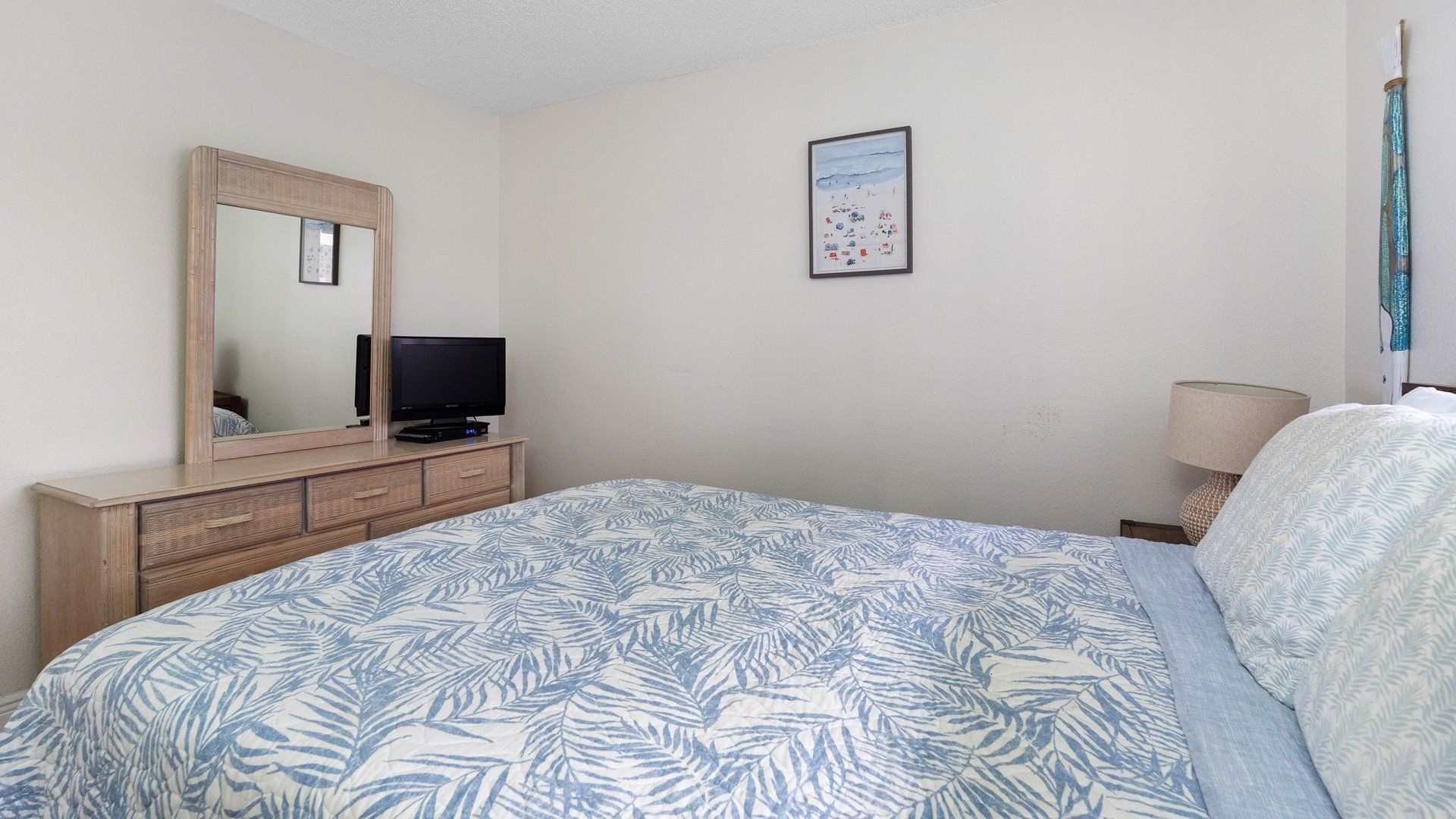 A bedroom with a bed, a dresser, a television, a framed picture on the wall, and a lamp.