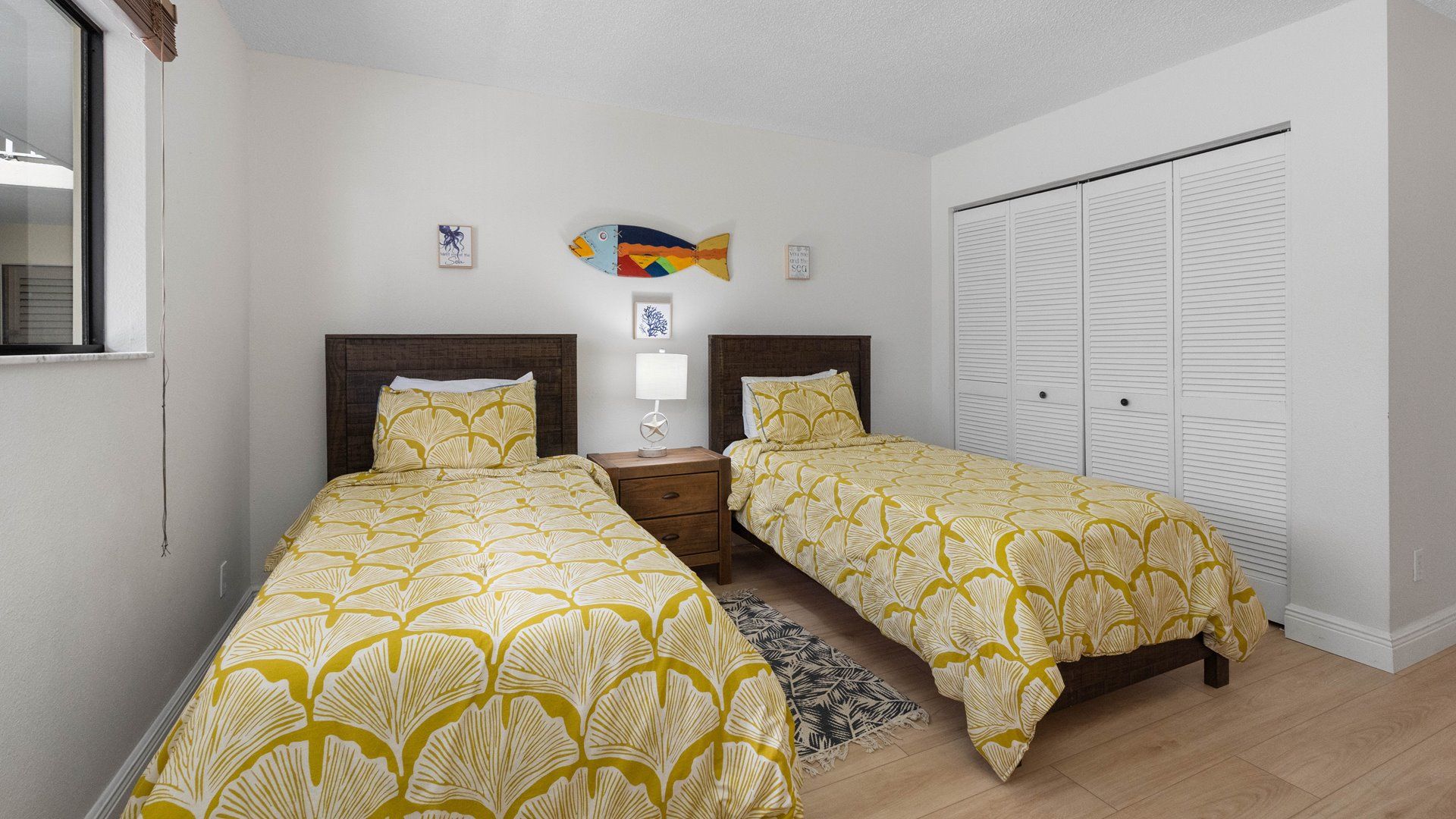 Une chambre avec deux lits, une table de chevet, une lampe, un petit élément de décoration murale et un placard.