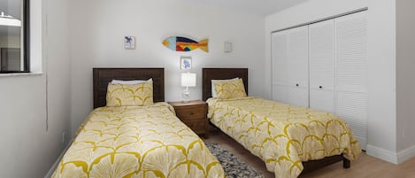 Une chambre avec deux lits, une table de chevet, une lampe, un petit élément de décoration murale et un placard.