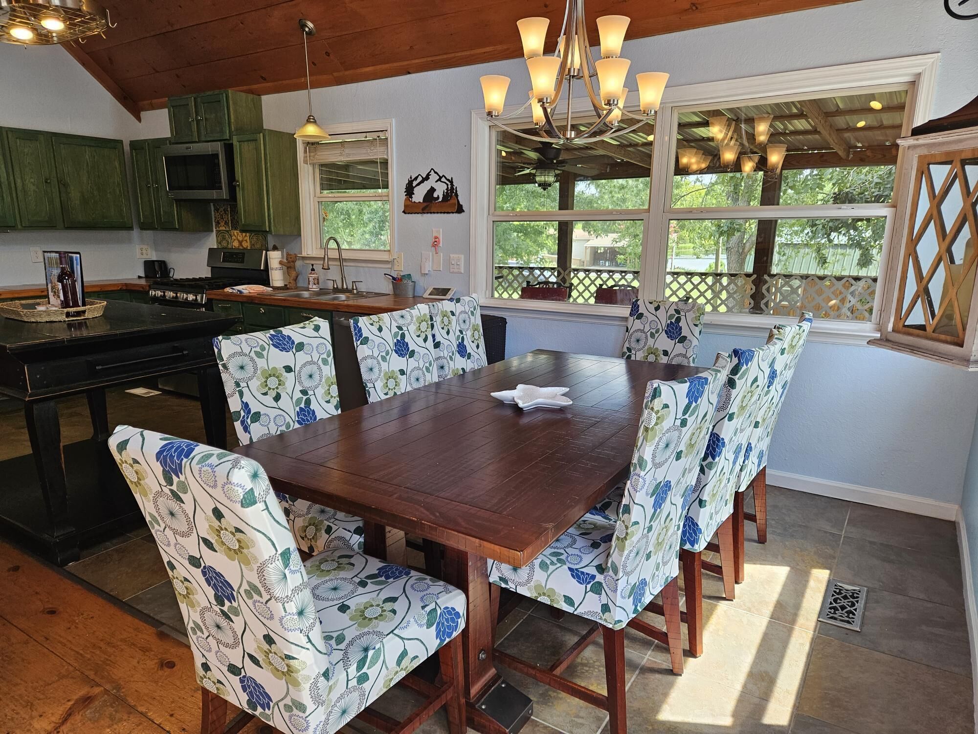 A dining area with a wooden table and floral-patterned chairs, a kitchen with green cabinets, and a chandelier.