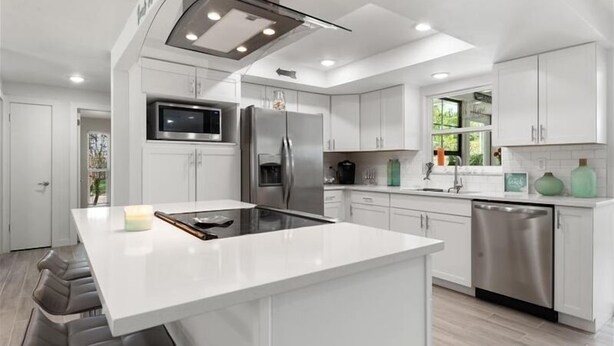 Una cocina moderna con armarios blancos, electrodomésticos de acero inoxidable y una isla central.