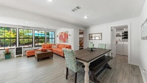 Un salón amplio con un gran ventanal, una mesa de comedor y un sofá naranja.