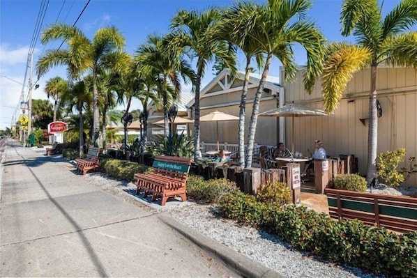 A beachfront restaurant with outdoor seating, palm trees, and a sign for 'Guppy's'.