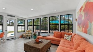 Una habitación amplia con un sofá grande color naranja, una mesa de centro de mimbre y vistas a una piscina a través de amplias ventanas.