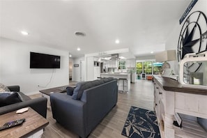 A modern living room with a grey sofa, a wooden coffee table, and a flat-screen TV mounted on the wall.