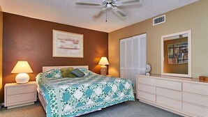 A bedroom with a bed, two bedside tables with lamps, a ceiling fan, a dresser, a window with blinds, and a framed picture on the wall. - Gulf Front Corner Unit & Million Dollar Views~ Chb305 (Madeira Beach)