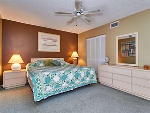 A bedroom with a bed, two bedside tables with lamps, a ceiling fan, a dresser, a window with blinds, and a framed picture on the wall. - Gulf Front Corner Unit & Million Dollar Views~ Chb305 (Madeira Beach)