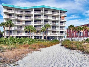 A multi-story hotel with balconies, a sandy pathway leading to the entrance, and palm trees. - Gulf Front Corner Unit & Million Dollar Views~ Chb305 (Madeira Beach)