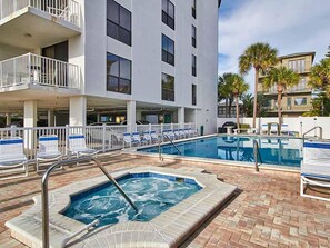 A hotel pool area with a hot tub, lounge chairs, and a building with balconies.