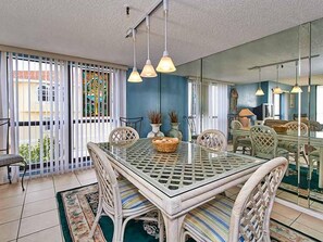 A dining area with a glass-top table, wicker chairs, and hanging pendant lights. - Gulf Front Corner Unit & Million Dollar Views~ Chb305 (Madeira Beach)
