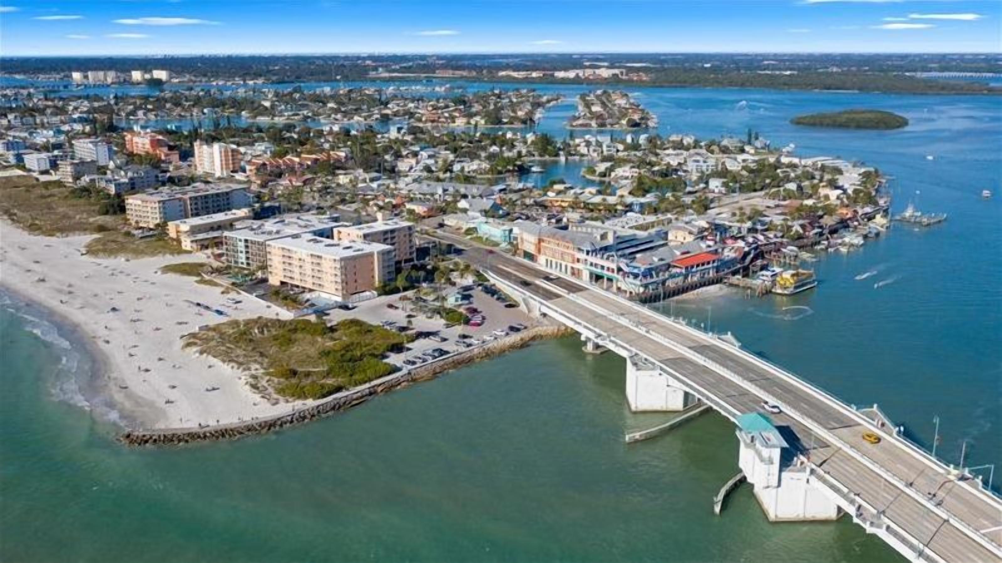 An aerial view of a coastal town with a prominent bridge connecting two land masses, a marina with boats, and a beach area.
