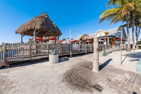 Zona de playa con valla de madera, sombrillas de paja y un edificio de fachada amarilla.
