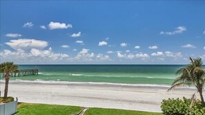 Une plage avec une jetée en bois qui s’avance dans l’océan, un ciel dégagé et quelques nuages.