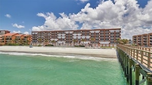 A beachfront hotel with multiple balconies, a pier, and a clear view of the ocean.