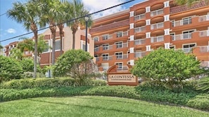 A multi-story building with balconies, surrounded by well-maintained greenery and palm trees.
