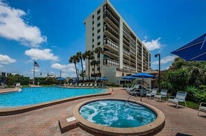 Un hotel con un amplio espacio de piscina, que incluye un jacuzzi, rodeado de tumbonas y sombrillas.