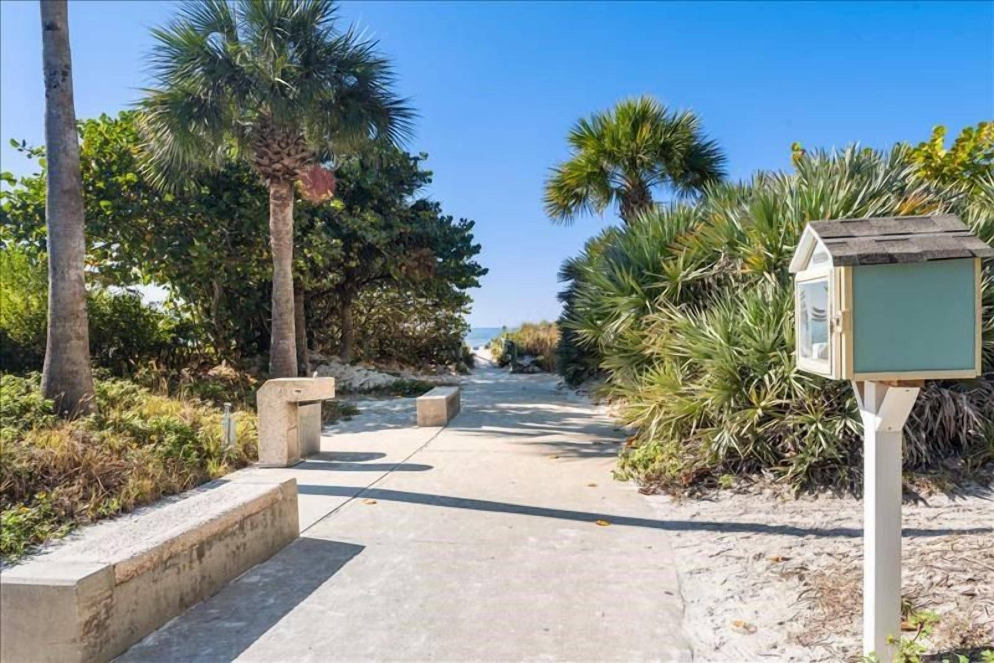 A pathway lined with palm trees and a small structure, likely a kiosk or information point, on a sunny day.