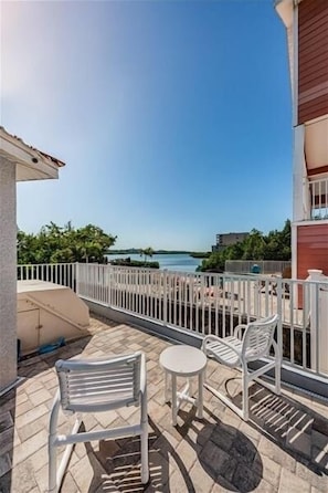 A balcony with white metal chairs and a small round table, overlooking a body of water and greenery.