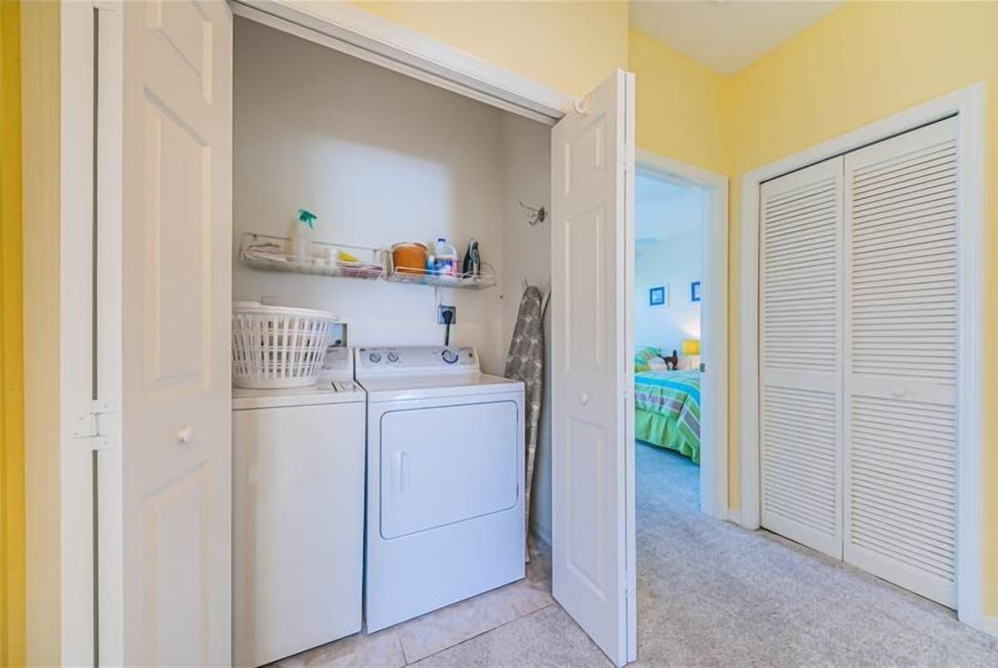 A laundry room with a washing machine and dryer, a basket, and shelves with cleaning supplies.
