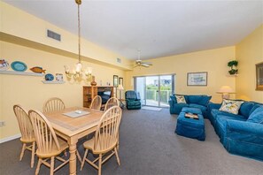 Uma sala de estar com uma mesa de jantar, cadeiras, um sofá azul e um ventilador de teto.
