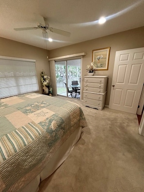 A bedroom with a large bed, a dresser, a ceiling fan, and a sliding glass door leading to a patio.