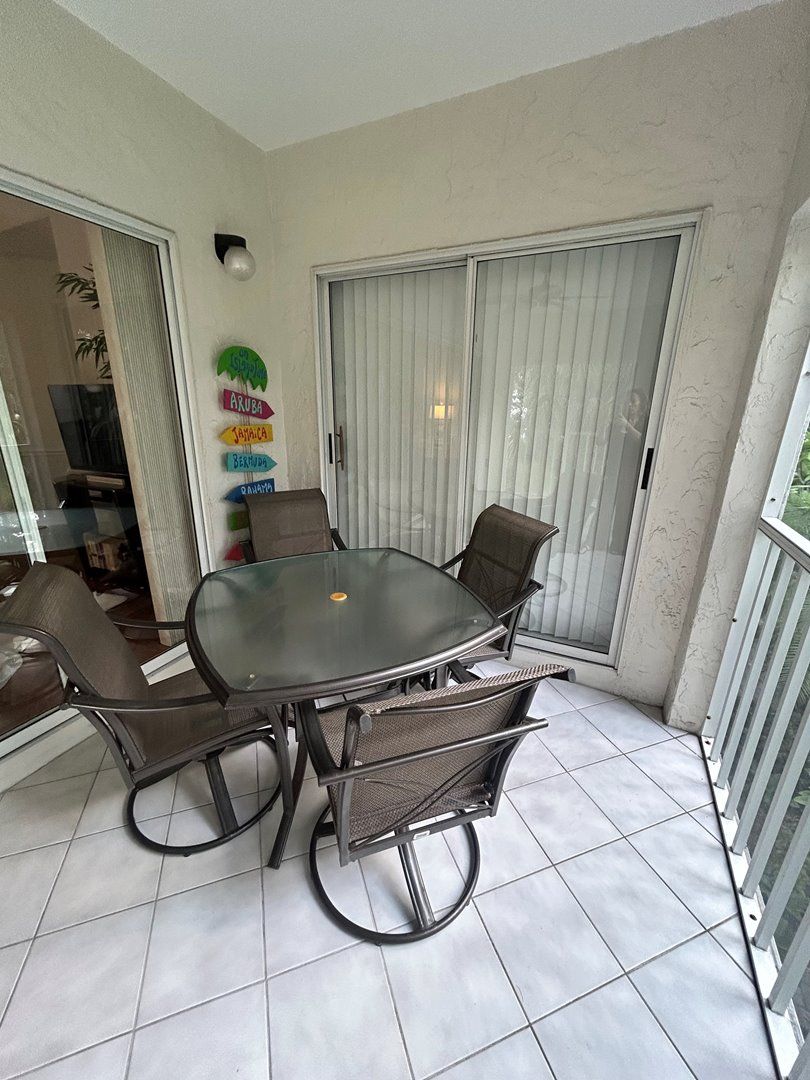 A dining area with a glass-top table and four chairs, a sliding glass door, and a wall with colorful name tags.