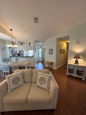 A spacious living room with a beige sofa, a dining area with a table and chairs, a kitchen in the background, and a hallway leading to another room. - Amazing Location at the Ship Watch Yacht & Tennis Club 3 month rental~ Ship1815 (Largo)