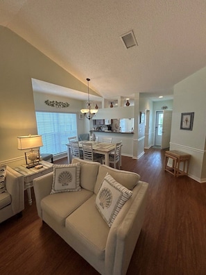 A spacious living room with a beige sofa and a dining area with a table and chairs.