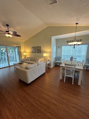 A spacious living room with a large sofa, a dining table with chairs, and a ceiling fan.