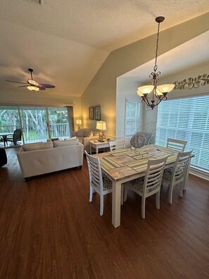 A dining area with a wooden table and white chairs, a white sofa, and a ceiling fan.