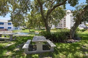 A picnic table in a grassy area with trees and a building in the background.
