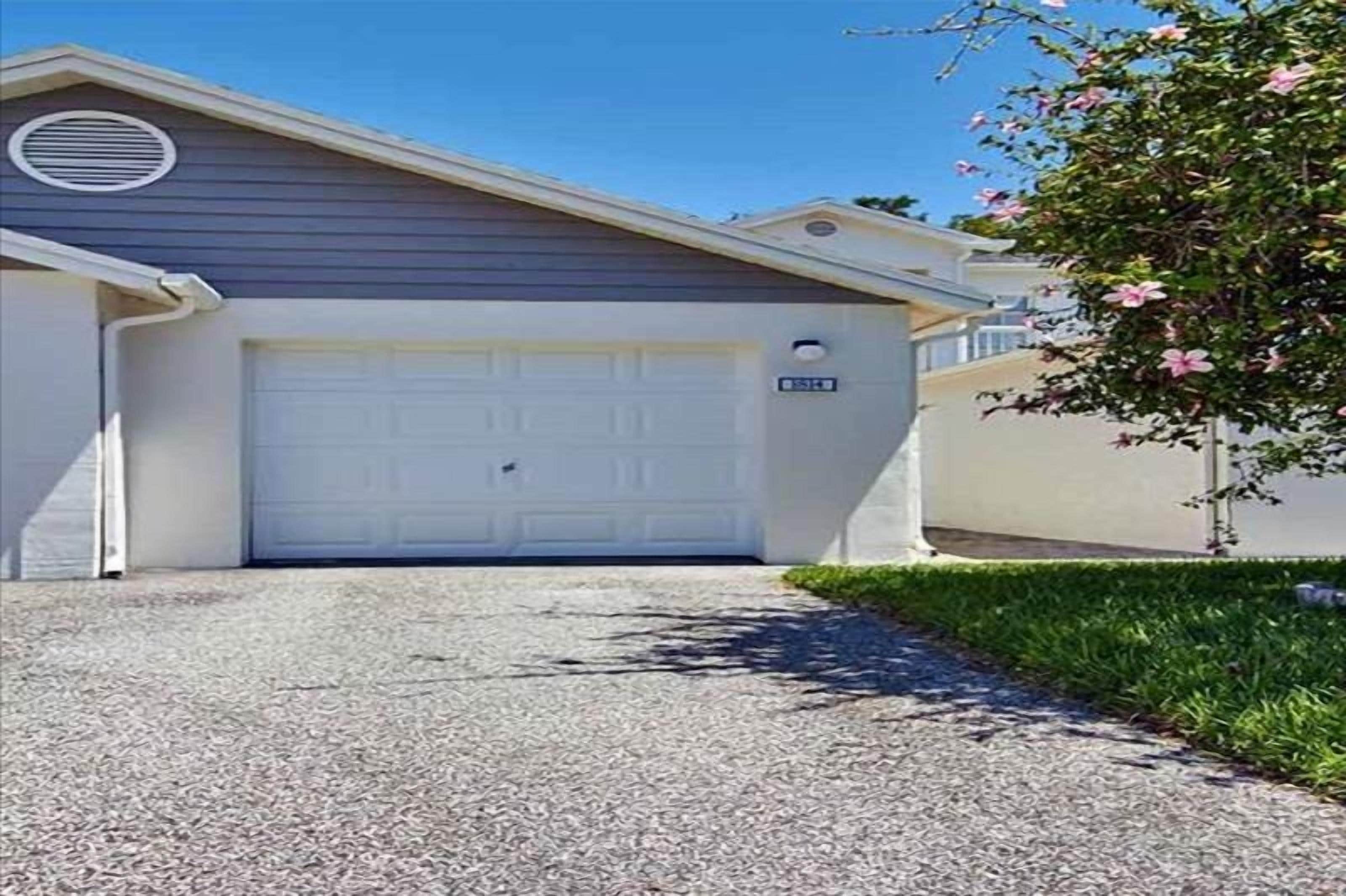 A residential garage with a white door, a small sign above the door, and a tree with pink flowers to the right.