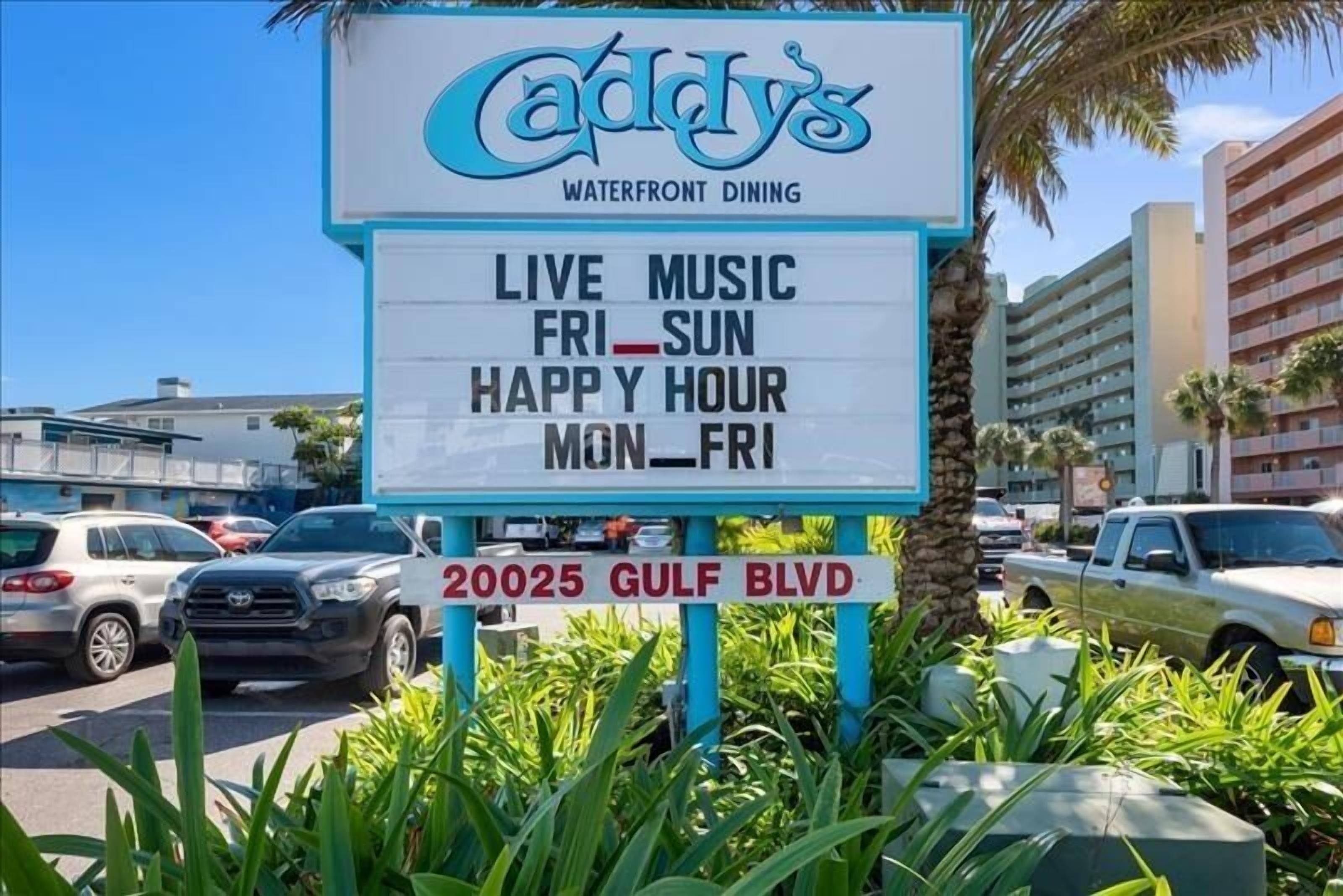 A sign for Caddy's Waterfront Dining with live music on Friday and Sunday, happy hour on Monday to Friday, and the address 20025 Gulf Blvd.