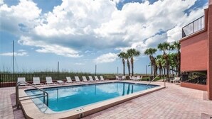A rectangular swimming pool with a tiled deck, surrounded by lounge chairs and palm trees.