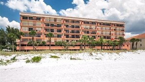 A multi-story hotel with a flat roof, numerous windows, and a sandy beachfront.