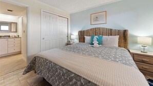 A bedroom with a large bed, a nightstand, a dresser, and a door leading to a bathroom.