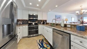 A modern kitchen with stainless steel appliances, white cabinetry, a marble countertop, and a decorative rug.