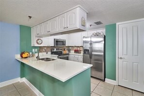 A kitchen with white cabinets, a stainless steel refrigerator, a microwave, and a sink. - Pet Friendly, Direct Gulf Front Condo with Million Dollar Panoramic Views! ~ TP404 (Indian Shores)