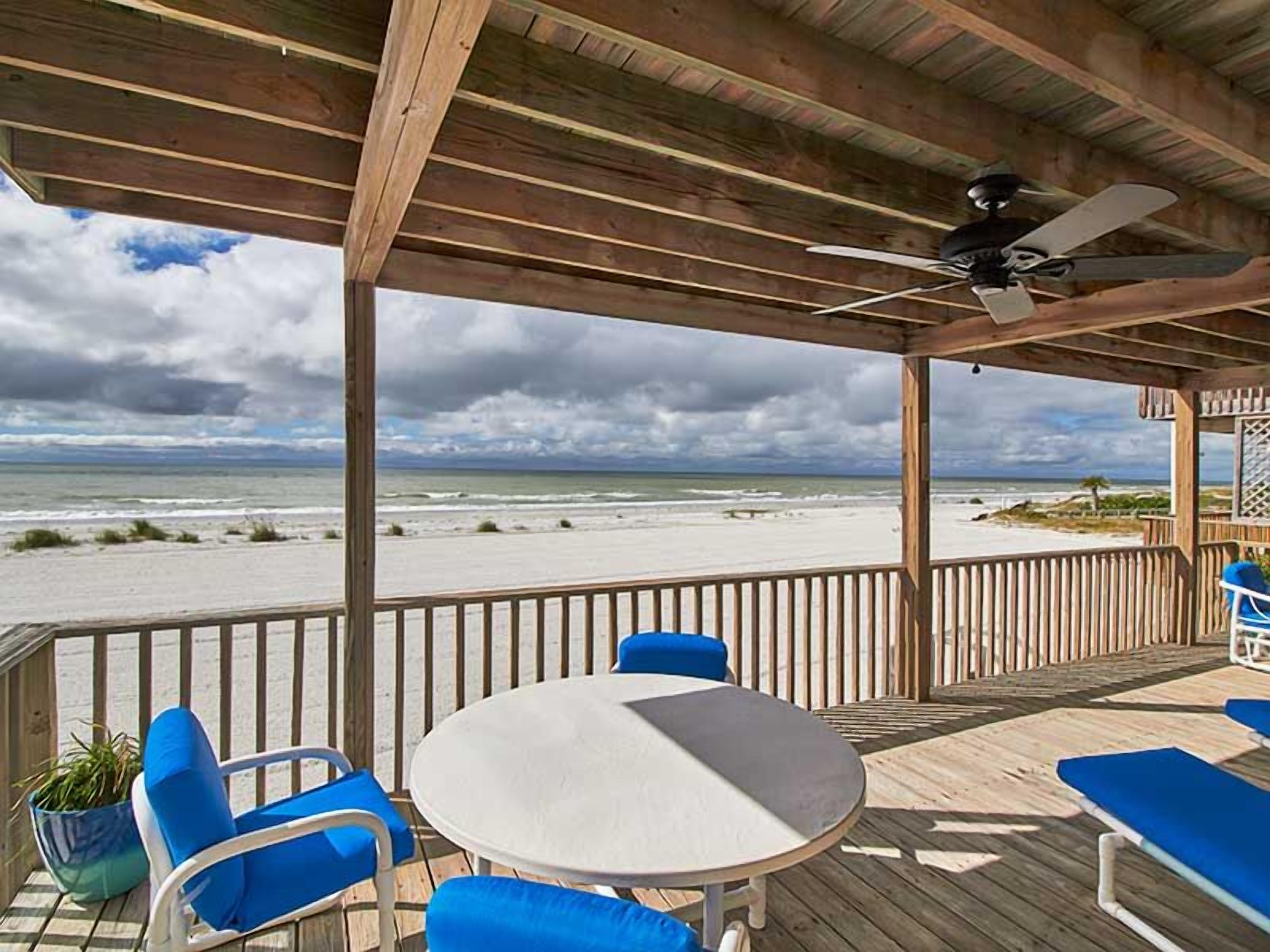 A covered outdoor seating area with a table and chairs, overlooking a beach.