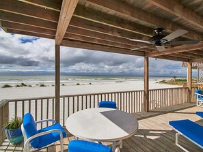 A covered outdoor seating area with a table and chairs, overlooking a beach.