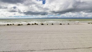 En strand med en bred sandstrand och utsikt över havet under en molnig himmel.