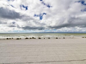 Une plage avec une vaste étendue de sable et une vue sur l’océan, sous un ciel nuageux.