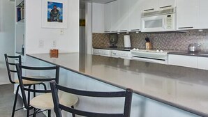 A modern kitchen with white cabinets, a built-in microwave, and a bar area with bar stools.