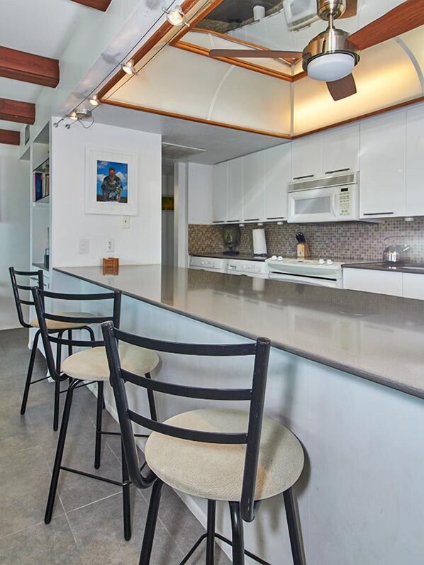 Una cocina moderna con armarios blancos, microondas integrado y una barra con taburetes.