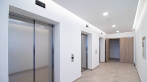 Un pasillo moderno con tres ascensores y una puerta de madera al final.
