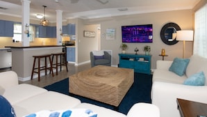 A modern living room with a sofa, ottoman, and a kitchen area in the background. - Tropical oasis (Lake Worth)