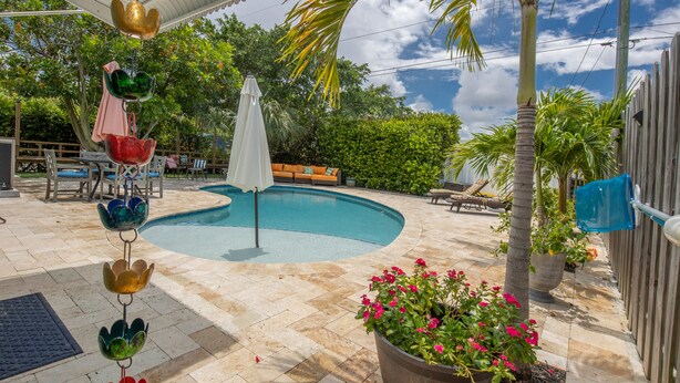 A swimming pool with a curved edge, surrounded by a patio area with chairs and a table. - Tropical oasis (Lake Worth)